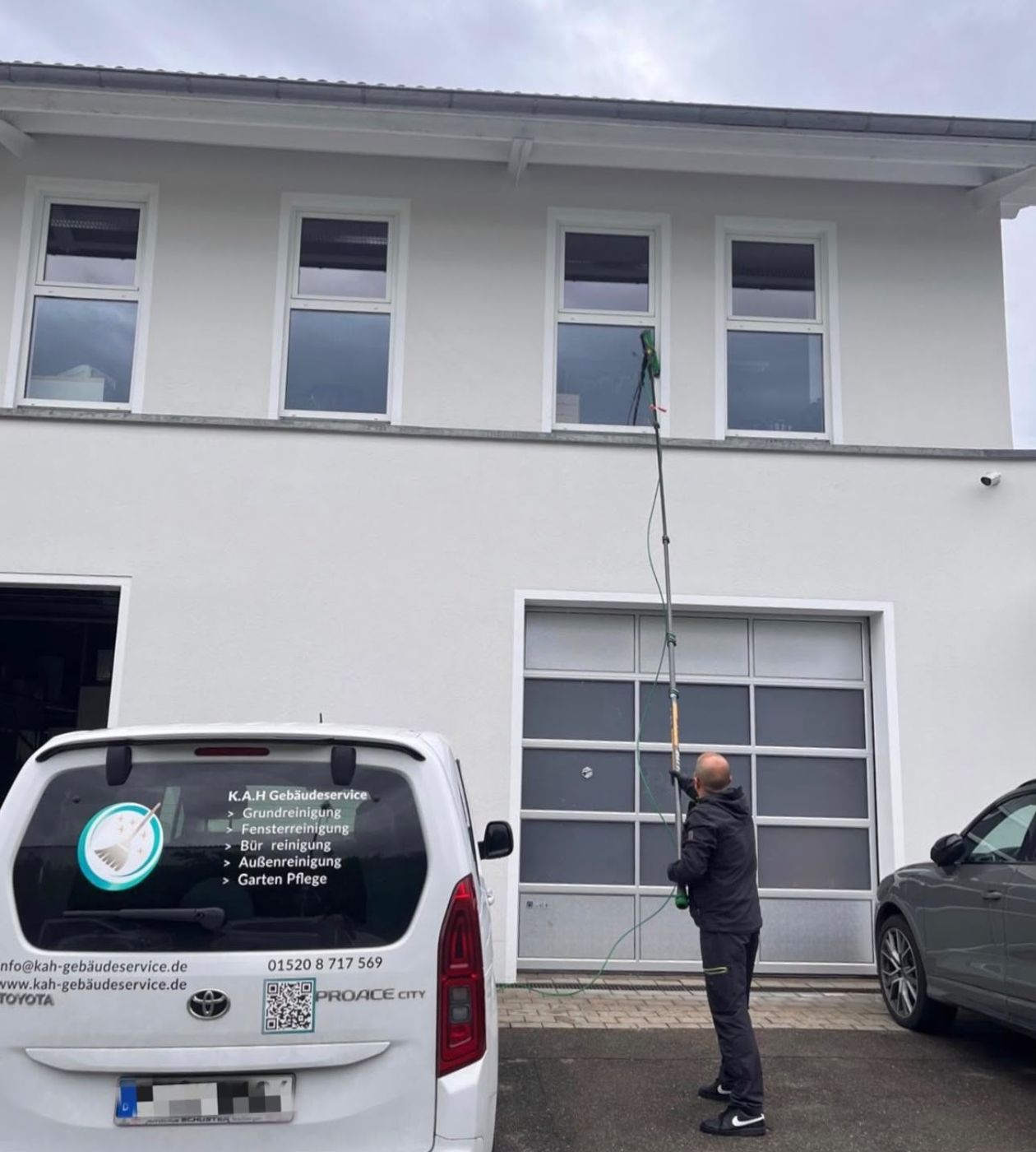 Mitarbeiter von K.A.H Gebäudeservice reinigt Fenster im Obergeschoss, davor der Firmenwagen